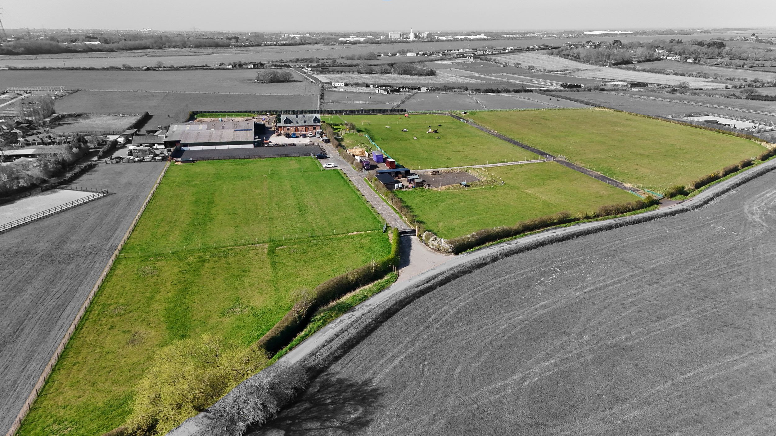 Aerial black and white photograph of agricultural land with buildings and green fields.