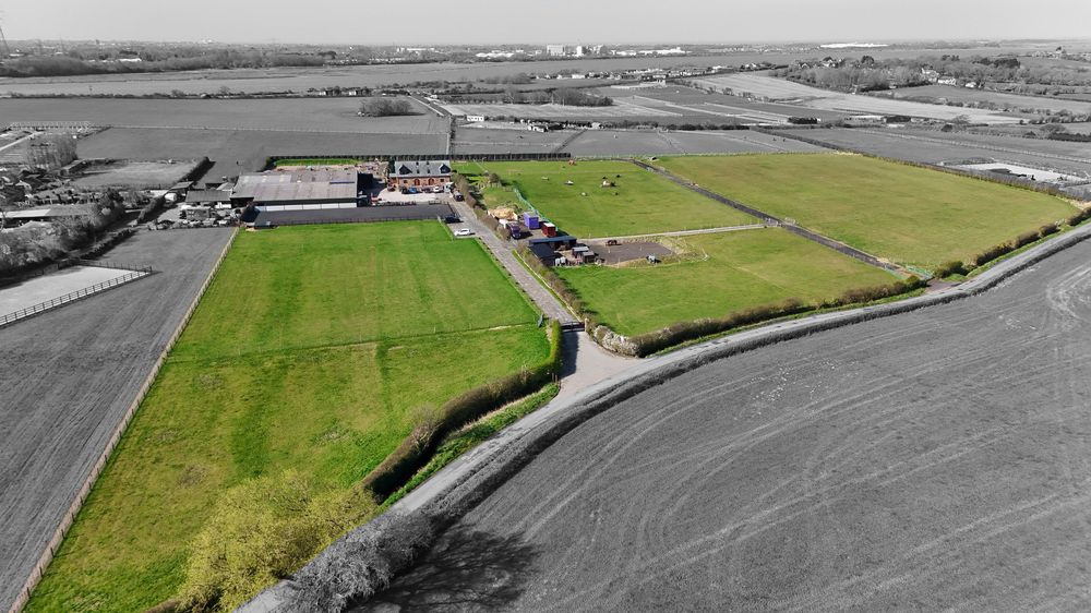 Aerial black and white photograph of agricultural land with buildings and green fields.