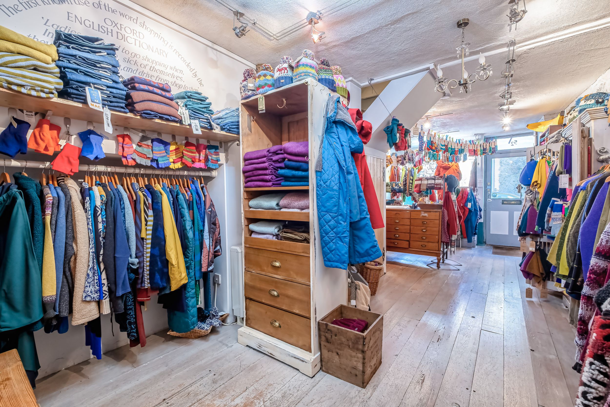 Wide angle view of a clothing boutique interior showing racks of apparel and wooden floors.