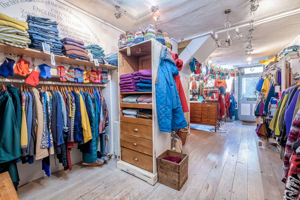 Wide angle view of a clothing boutique interior showing racks of apparel and wooden floors.