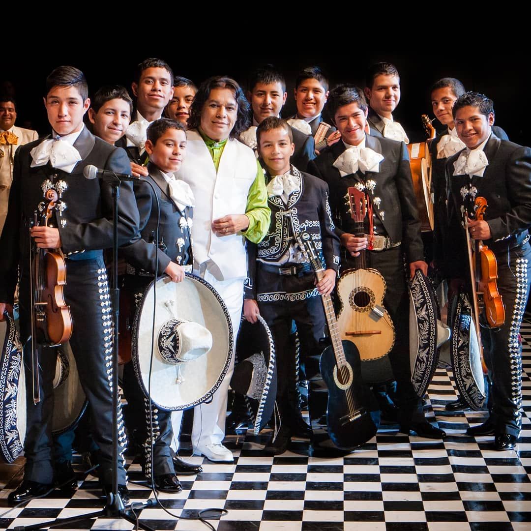 A mariachi band wearing traditional outfits poses with their instruments against a black and white checkered floor.