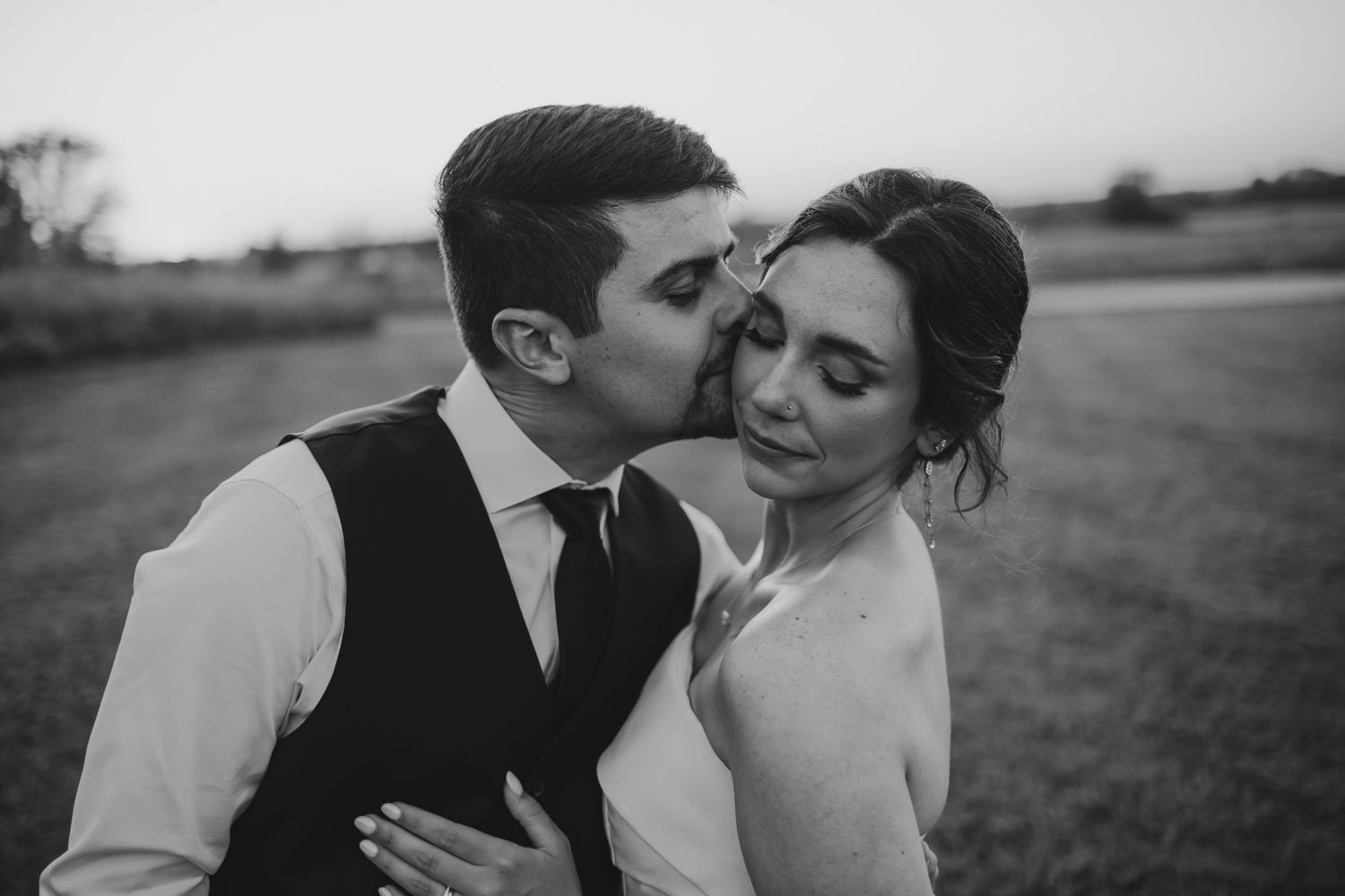 Groom kissing his bride at sunset in black-and-white located in Zionsville, Indiana