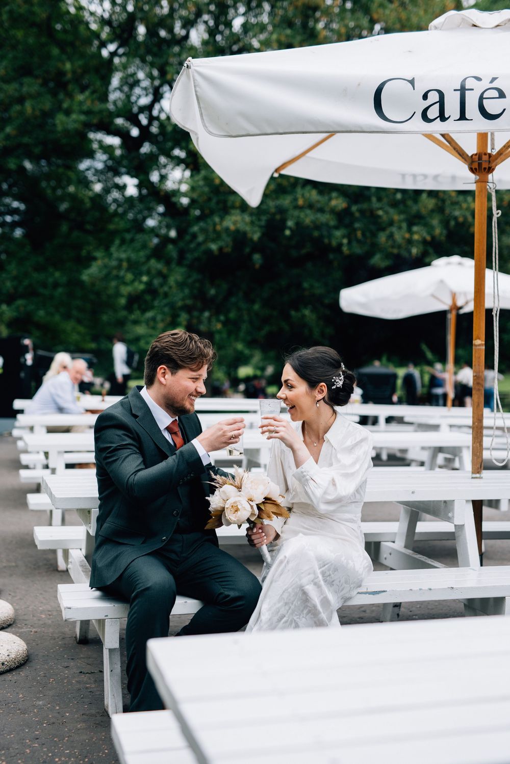 A newlywed couple shares an intimate moment at an outdoor cafe with white umbrellas.