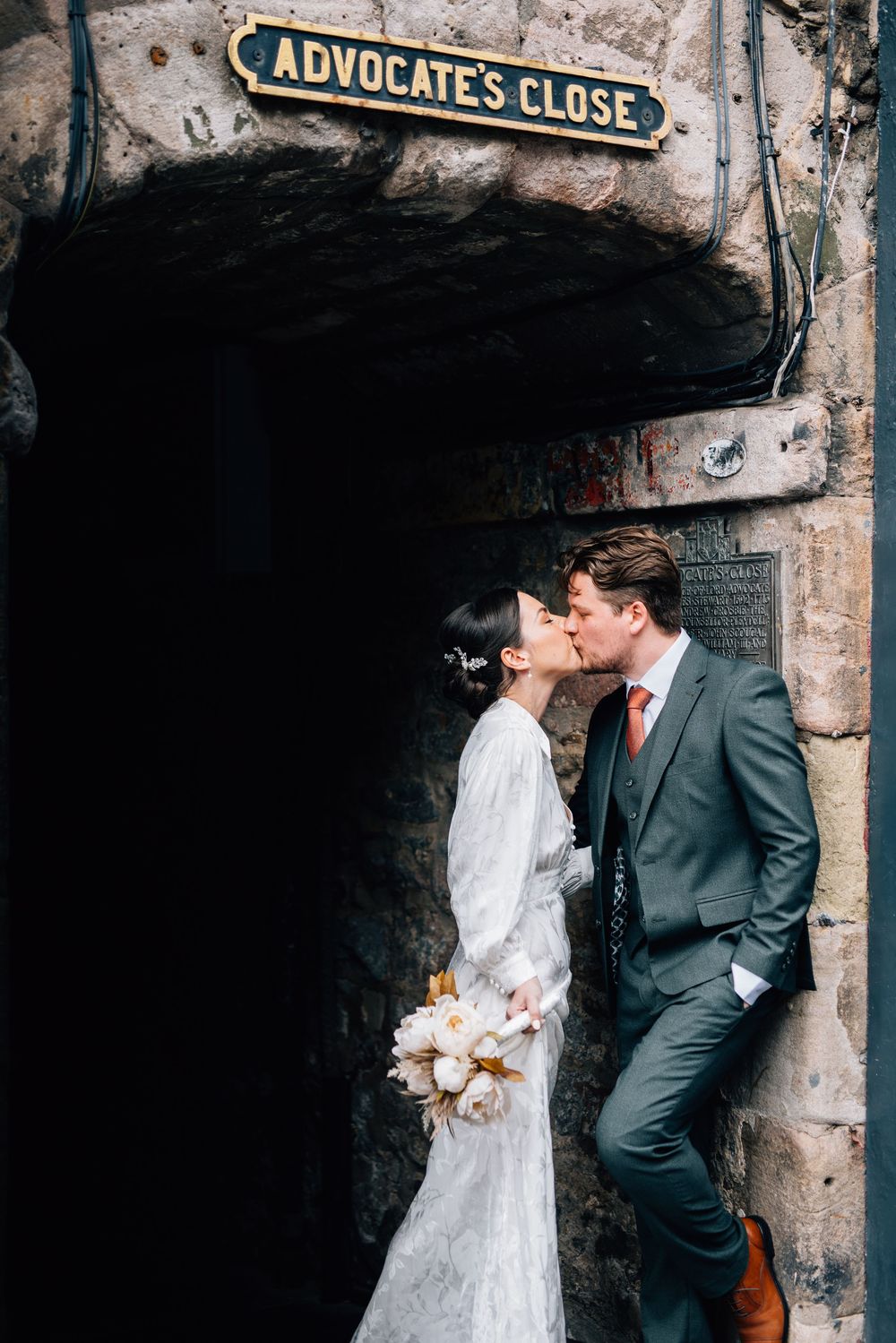A couple shares a romantic moment under the historic Advocate's Close sign in Edinburgh's Old Town.