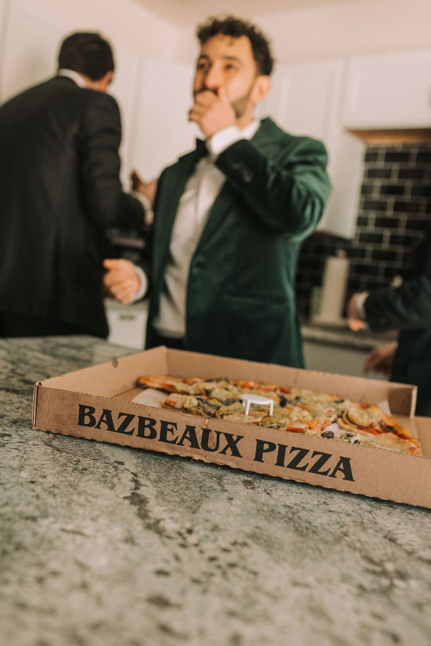 Pizza boxes labeled Bazbeaux Pizza sit on a granite counter at what appears to be a wedding reception.