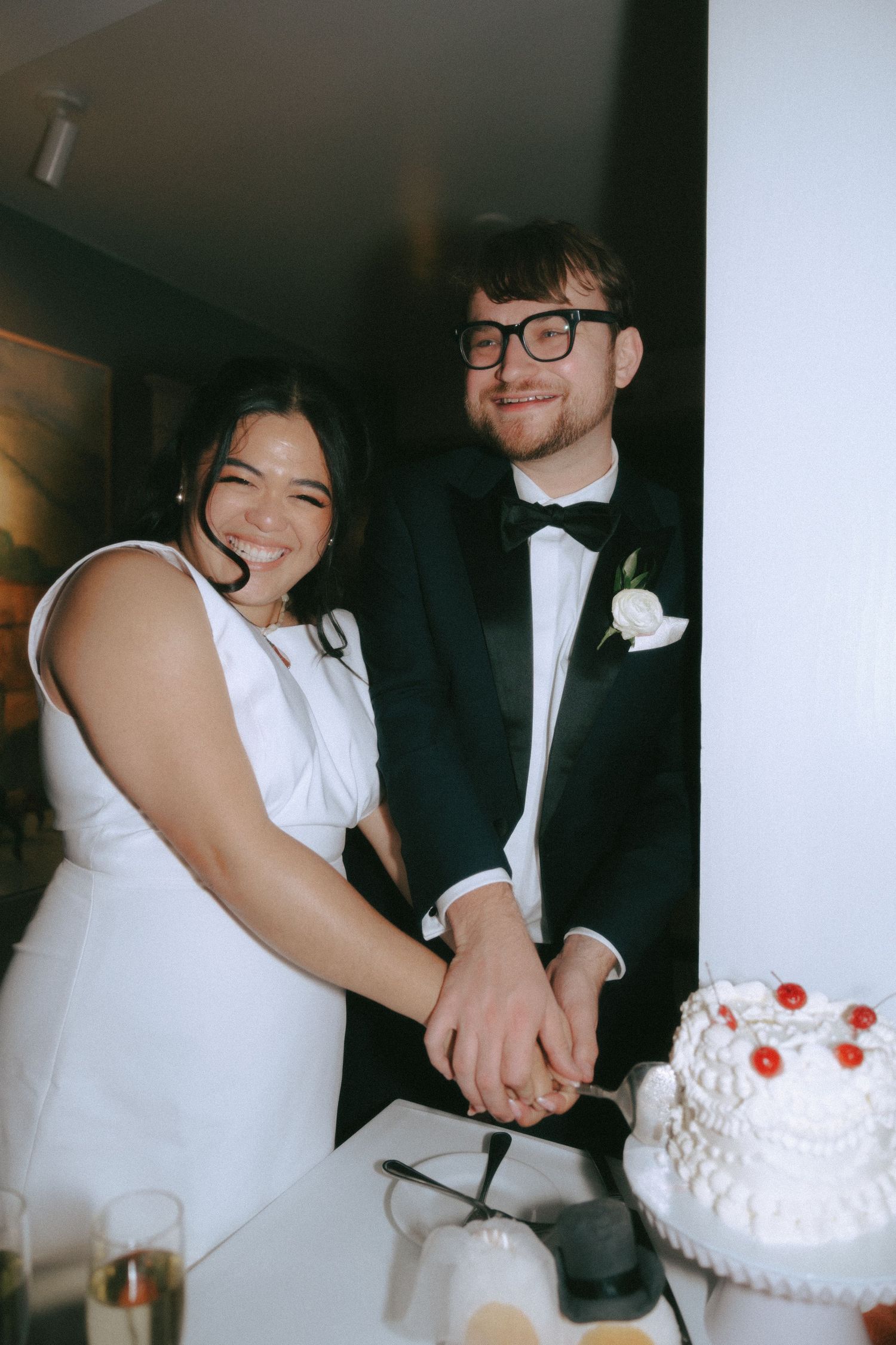 A couple in wedding attire cuts their white wedding cake together during their reception celebration.