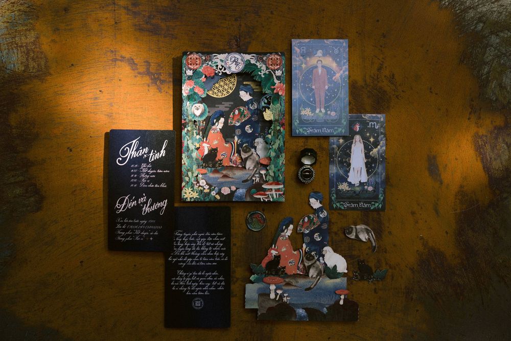 Artistic wedding invitation suite with dark moody lighting and decorative elements displayed on textured surface.
