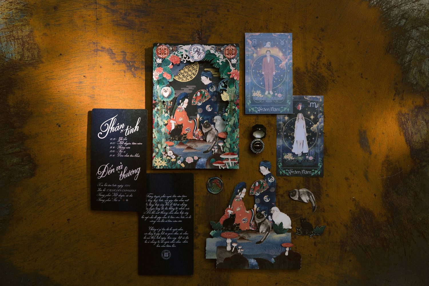 Artistic wedding invitation suite with dark moody lighting and decorative elements displayed on textured surface.