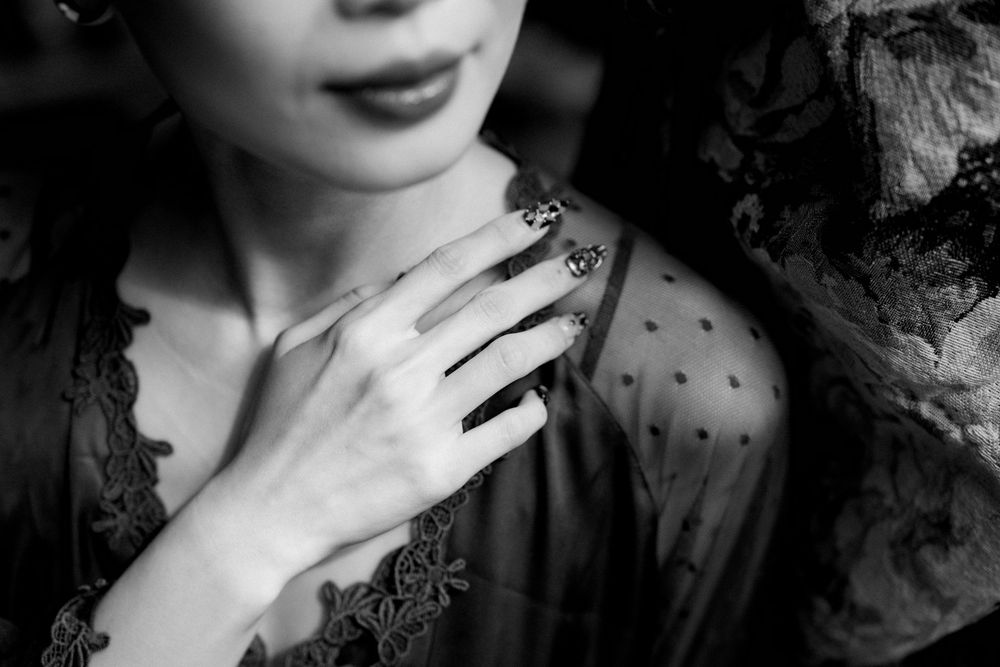 Black and white photo showing delicate hand with polished nails resting on sheer polka dot and lace fabric.