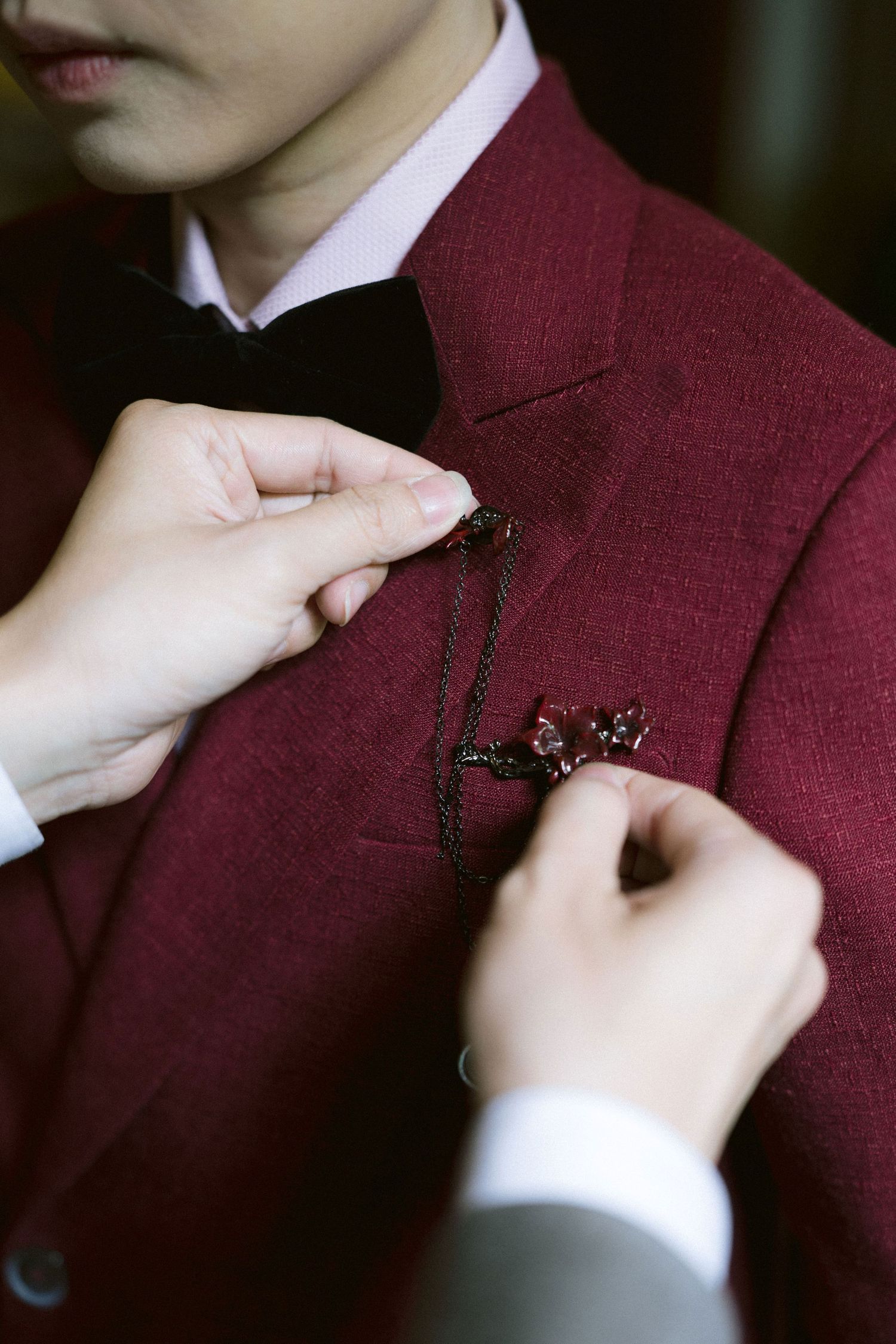 Close-up shots of hands pinning a decorative brooch onto a burgundy suit jacket.
