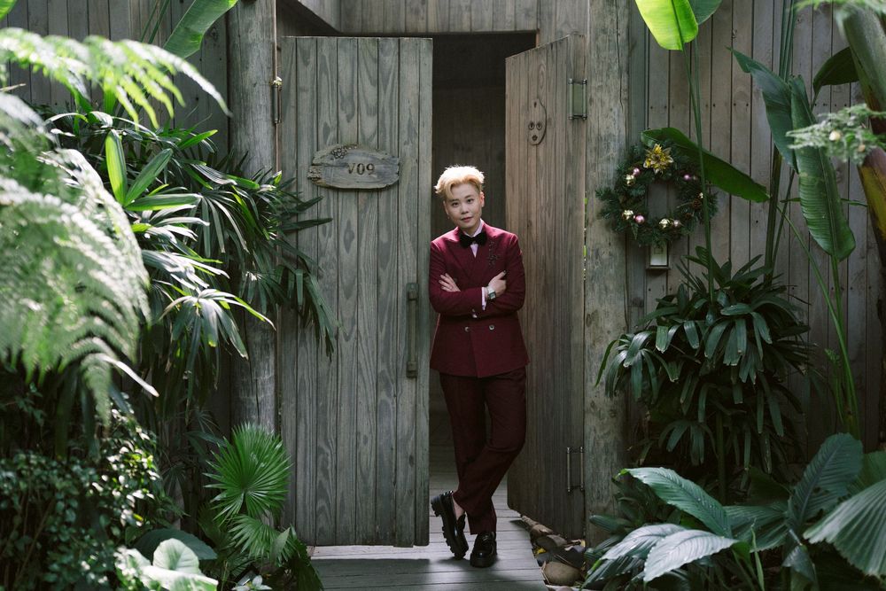 A figure stands in front of a rustic wooden door surrounded by lush tropical plants and greenery.