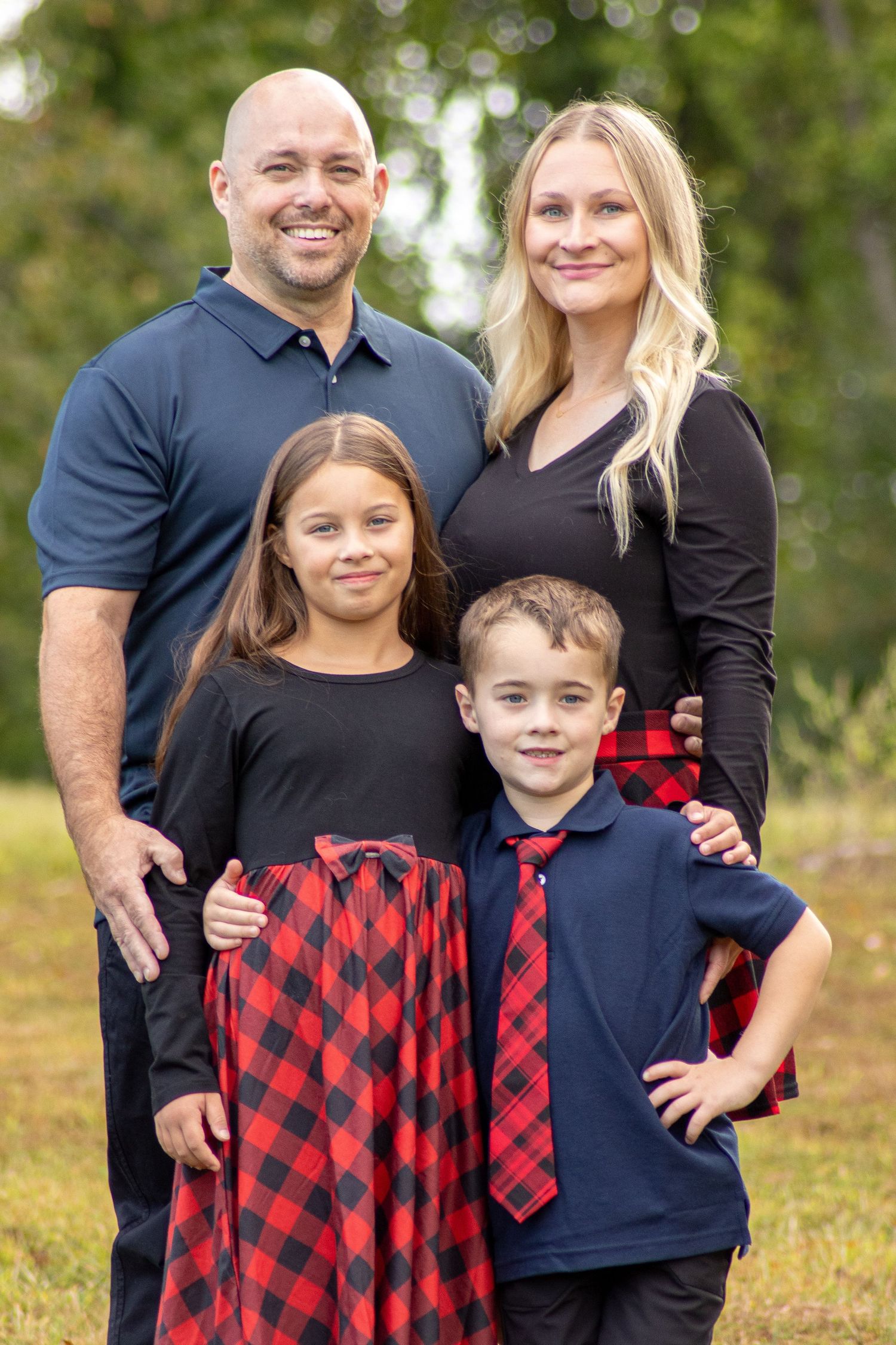 Family of four in coordinated outfits posing together in an outdoor park setting.