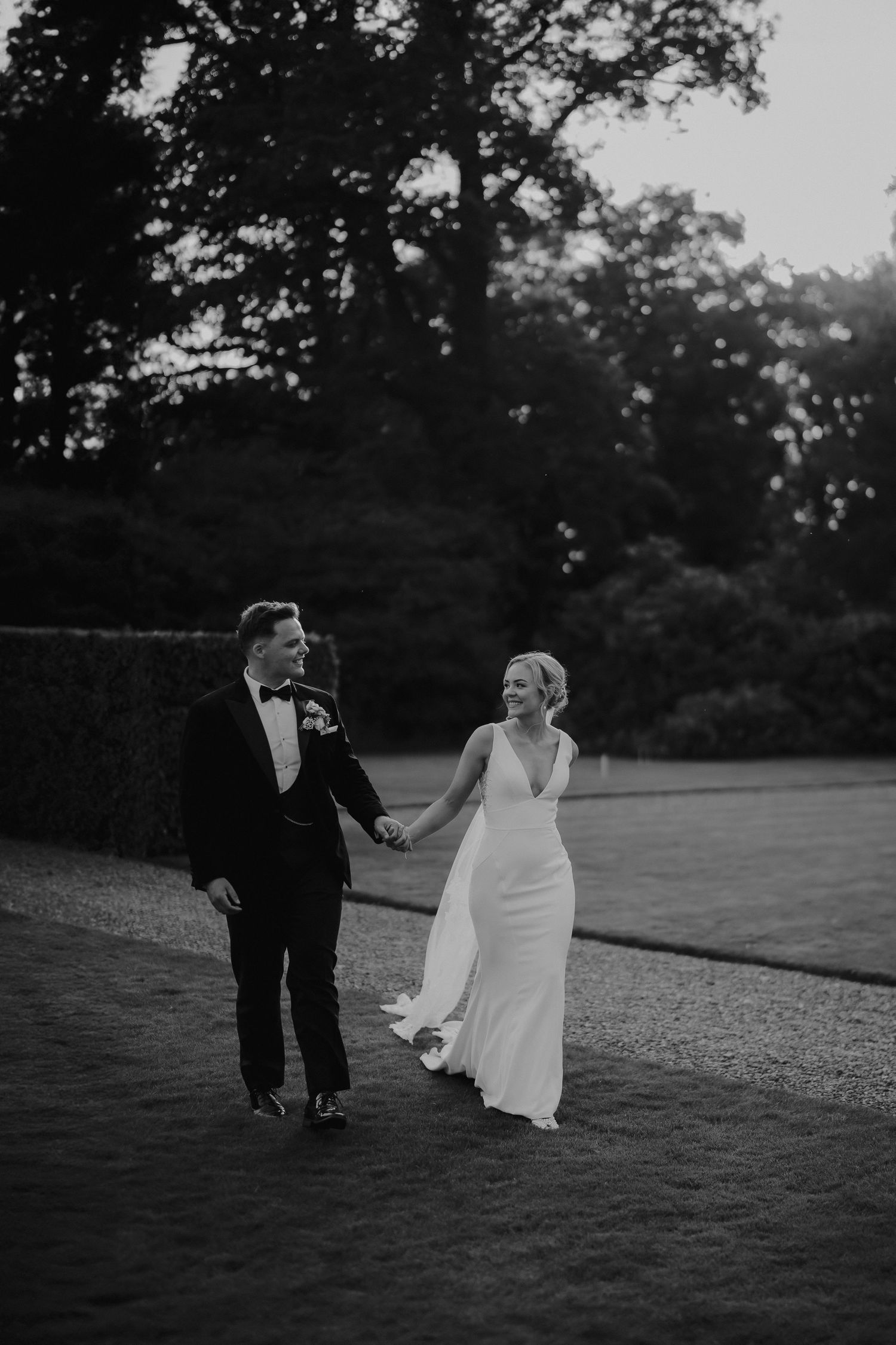 bride and groom walking across lawn during golden hour at Iscoyd park