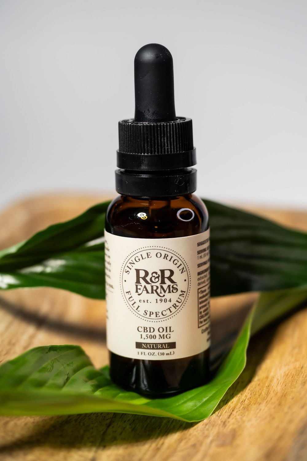 R&R Farms full spectrum CBD oil 1500mg natural flavor in an amber dropper bottle on wood.
