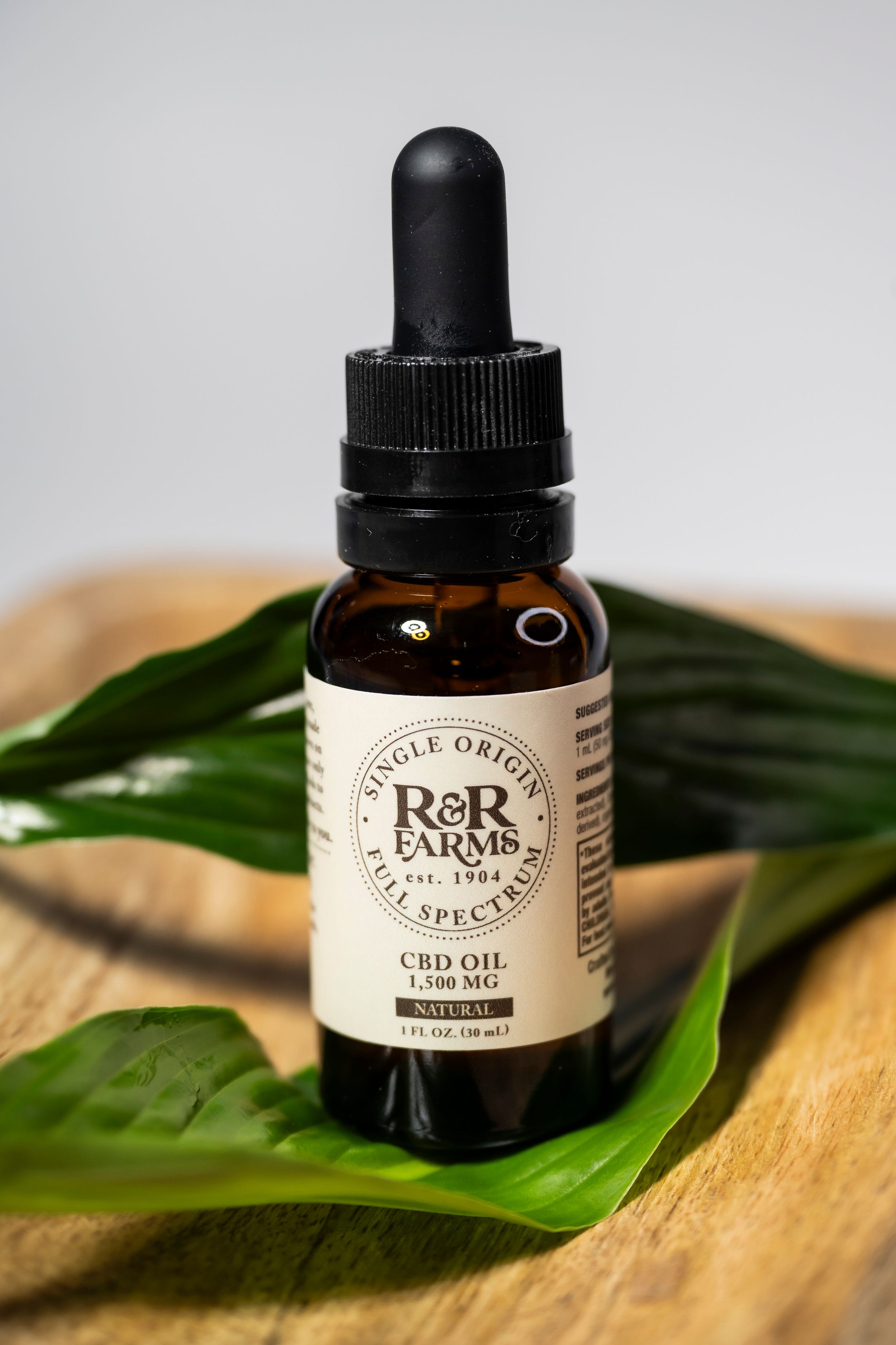R&R Farms full spectrum CBD oil 1500mg natural flavor in an amber dropper bottle on wood.