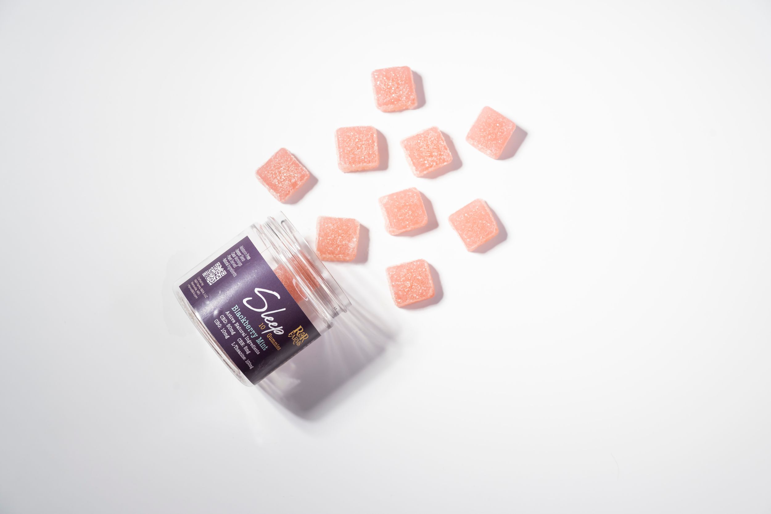 Pink CBD gummies spilling out of a small purple container on a white background.