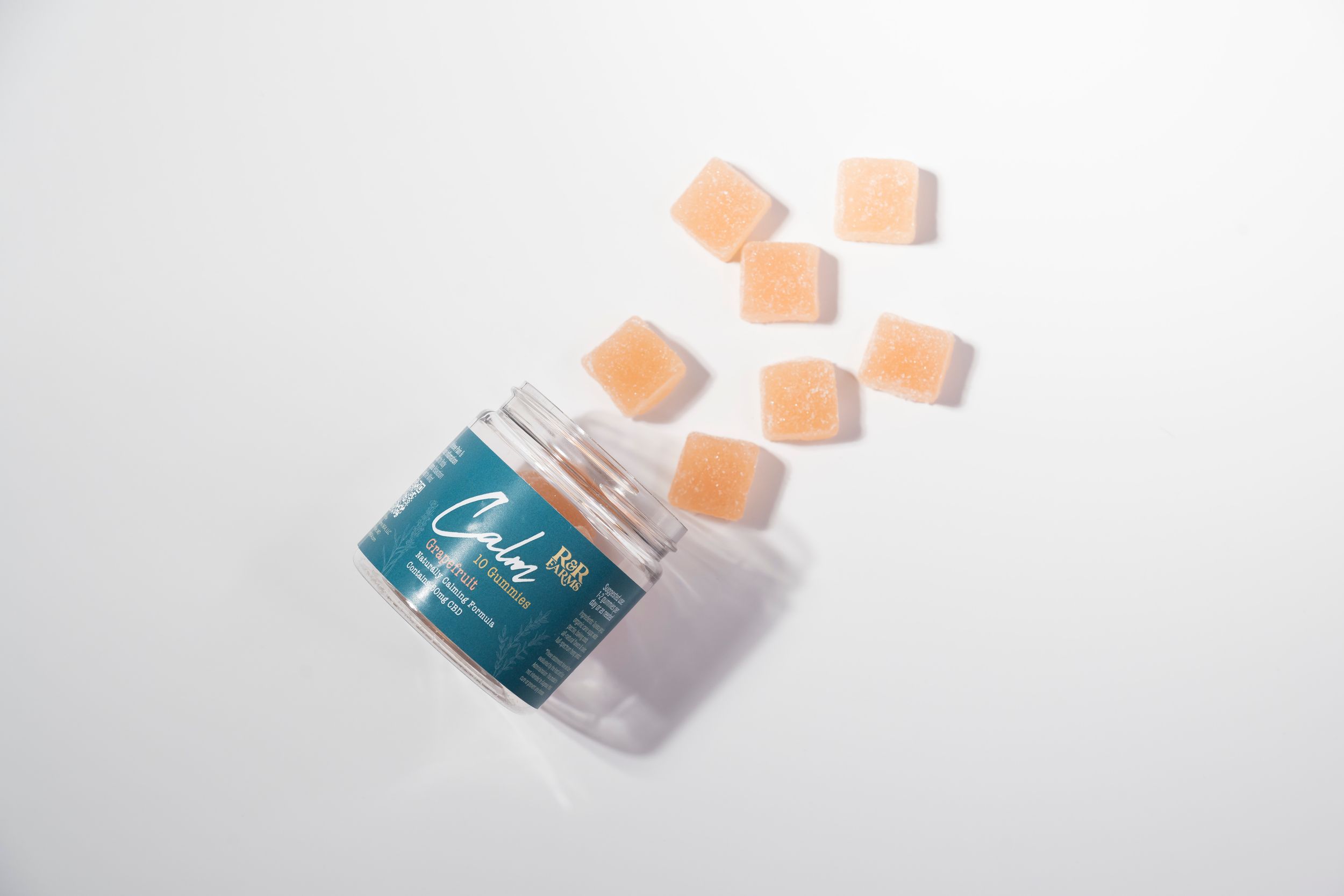 Peach CBD gummies spilling out of a teal jar onto a white surface.