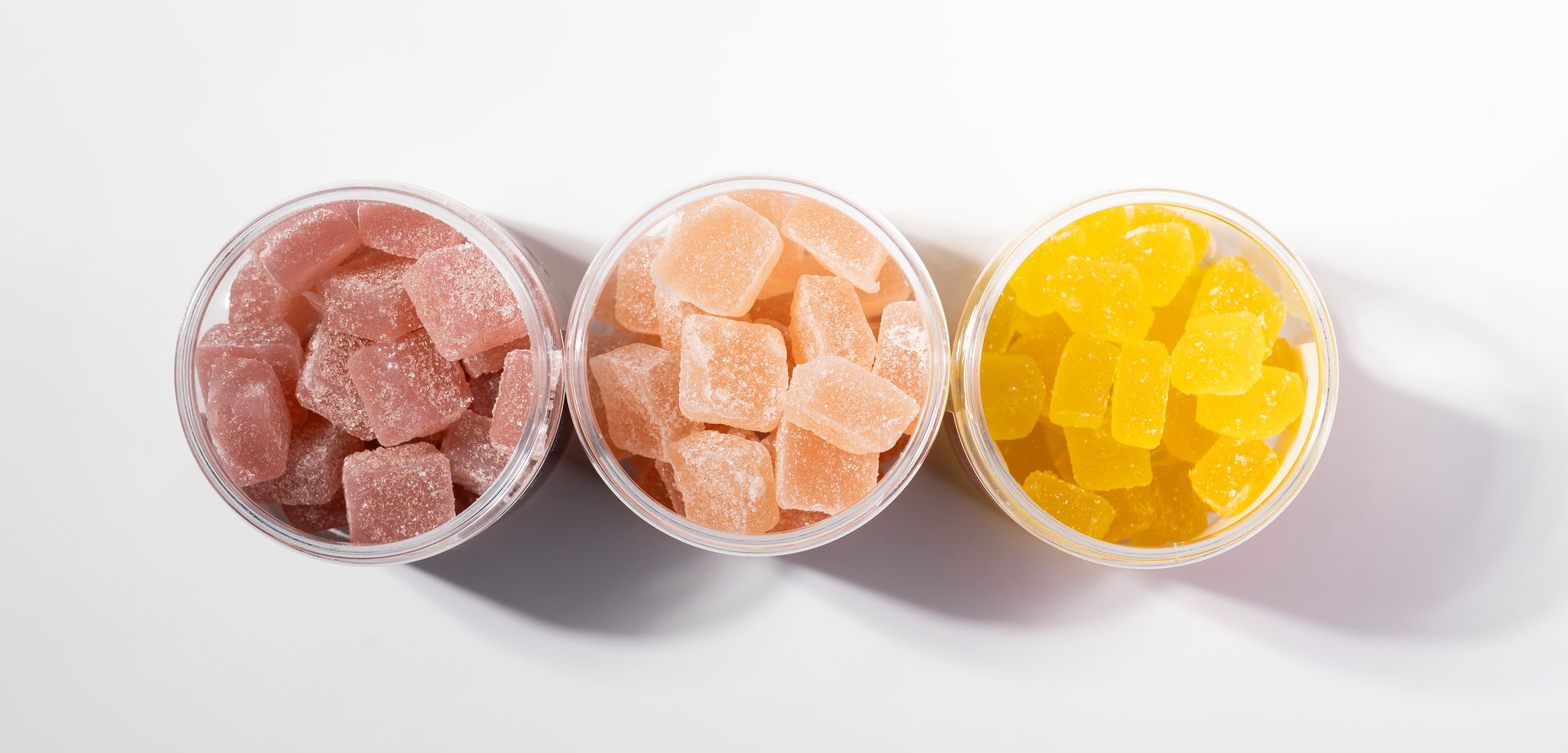 Three cups of assorted fruit gummies in pink, peach, and yellow flavors on white background.