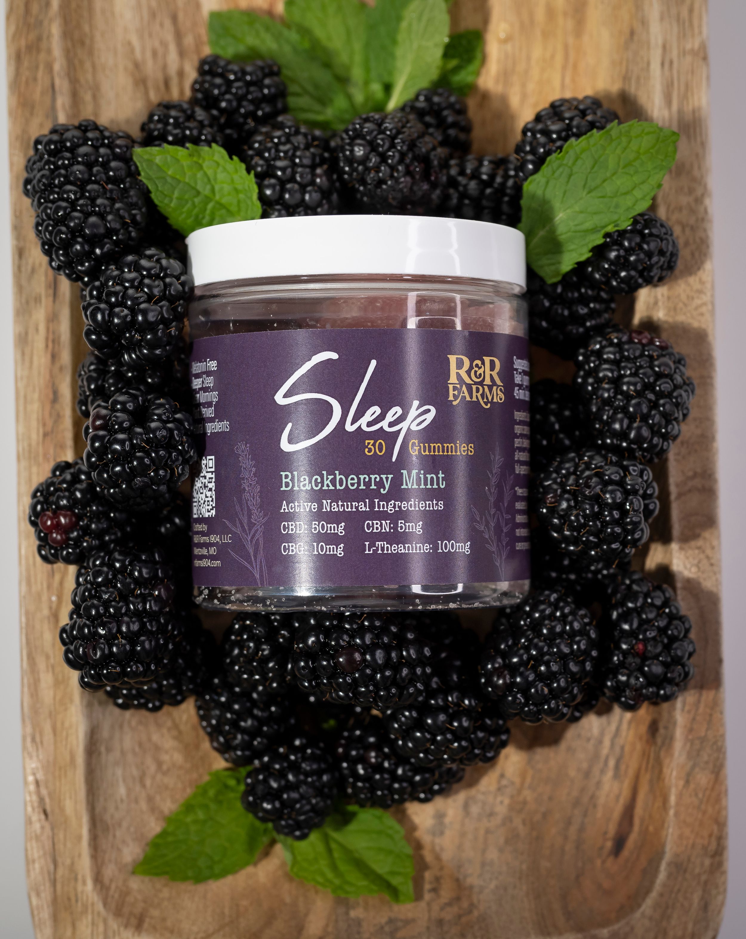 R&R Farms Sleep blackberry mint CBD gummies jar surrounded by fresh blackberries and mint leaves.