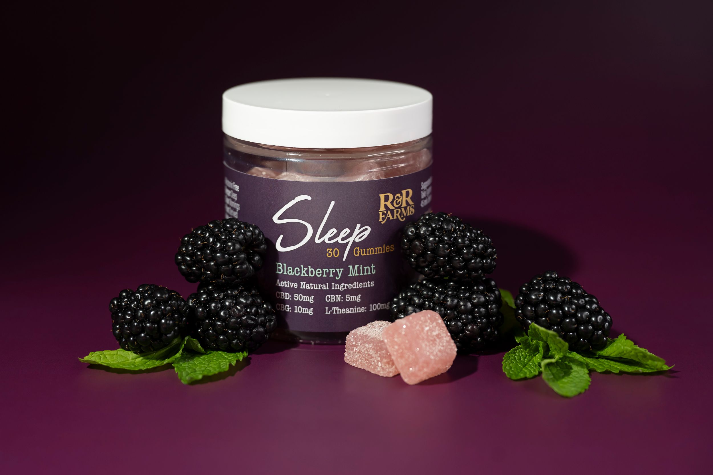 R&R Farms Sleep blackberry mint CBD gummies jar with fresh blackberries and mint on purple background.