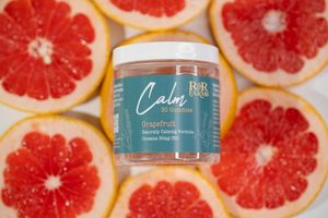 R&R Farms Calm Grapefruit CBD gummies jar centered among sliced grapefruits on white background.