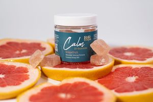 R&R Farms Calm Grapefruit CBD gummies jar with gummy bears and sliced grapefruits on pink background.