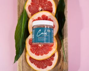 Calm CBD gummies jar in grapefruit flavor displayed on fresh grapefruit slices with tropical leaves on pink background.