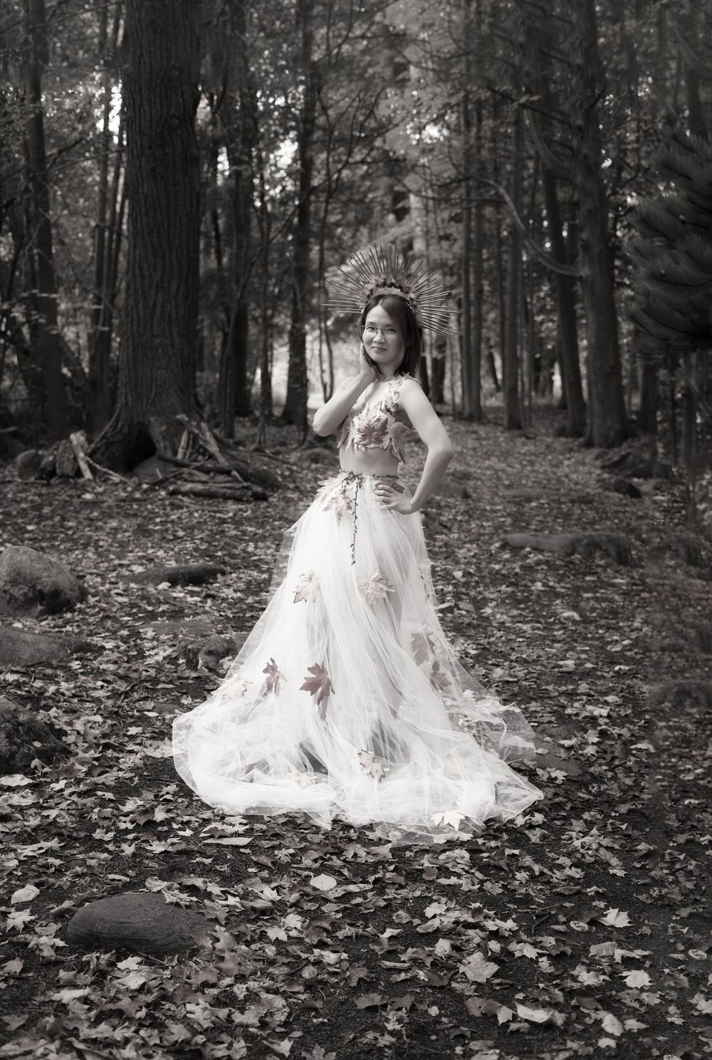 A figure in a flowing white dress poses gracefully among fallen autumn leaves in a misty forest setting.