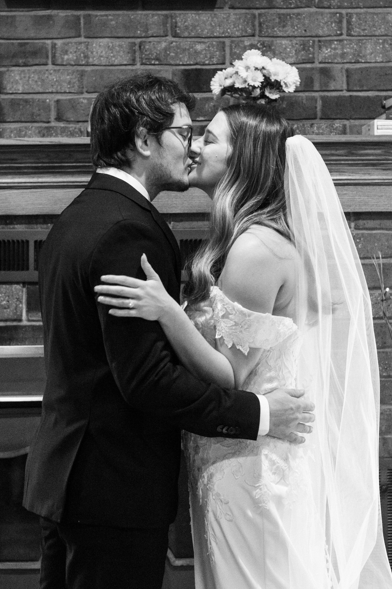 A romantic black and white wedding photo showing a tender kiss between newlyweds against a brick wall backdrop.
