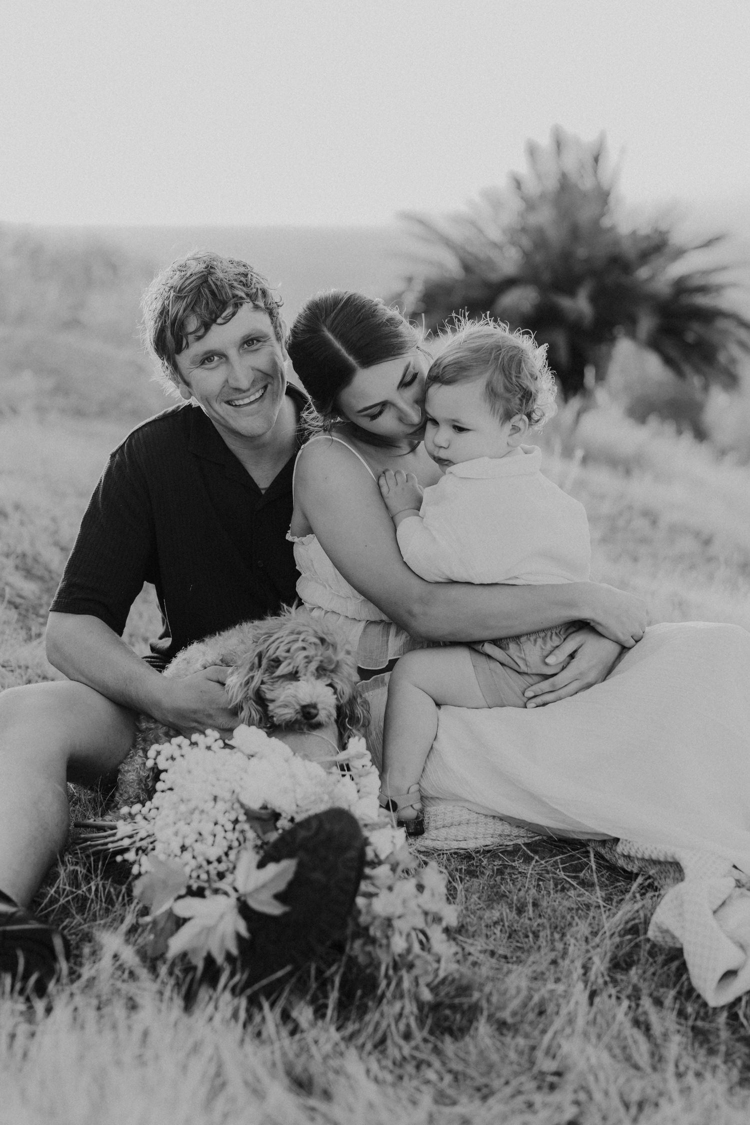 A romantic black and white photo sequence showing a couple laying in a field of flowers sharing tender moments together.