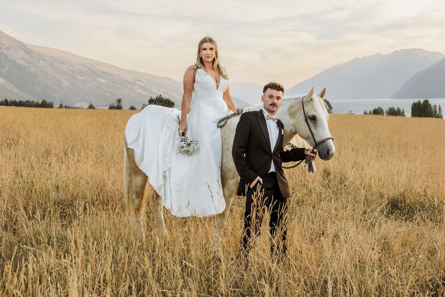 White horse standing in golden mountain field with dramatic mountain backdrop.