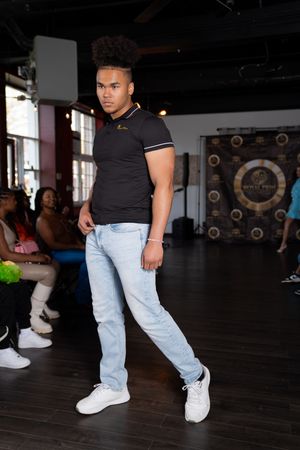 A dancer in light denim jeans and black top performs a sequence of dance moves on a dark wooden floor.