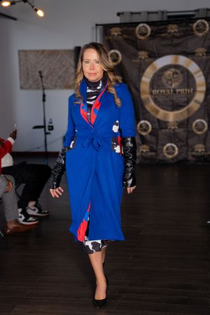 Fashion model showcases bright blue winter coat with red accents on dark runway.