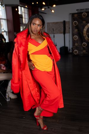Fashion model walks runway in vibrant red jacket and yellow top with dramatic styling at indoor fashion show.