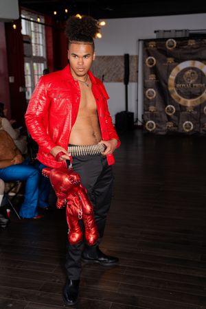 Performer in bright red jacket and black pants dances in studio space with wooden floors.
