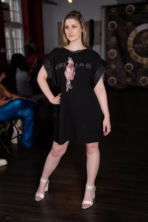 Model in black t-shirt dress and sparkly shoes poses on dark hardwood floor.