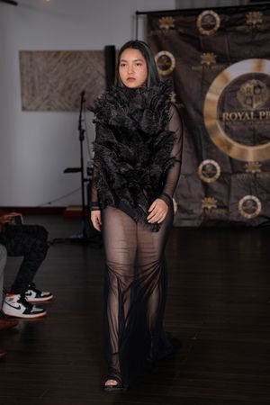 Model presents sheer black evening wear with dramatic ruffles on dimly lit fashion runway.