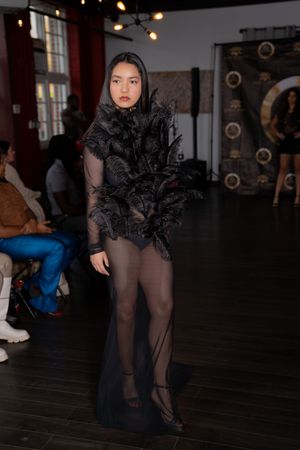 Dramatic black tulle dress with ruffled details shown on dimly lit runway.