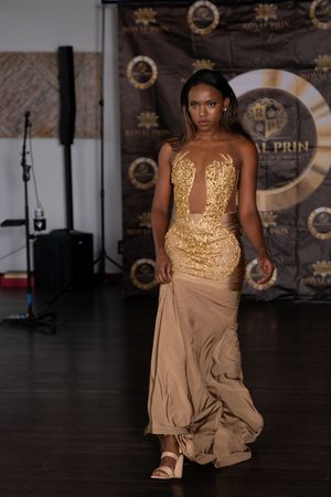 Model walks runway in stunning gold sequined bodice gown with flowing champagne skirt at fashion event.