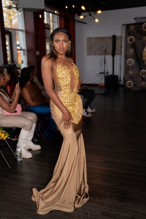 Dancer in flowing gold sequined top and beige skirt performs elegant movements on dark hardwood floor.