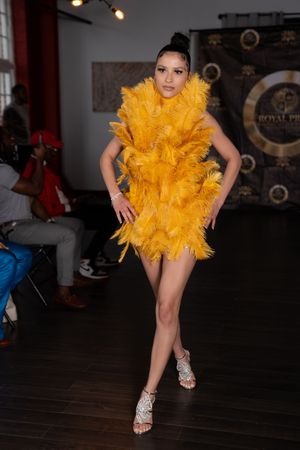 Dancer in bright yellow feathered costume and white shoes performs dynamic poses in dark studio setting.