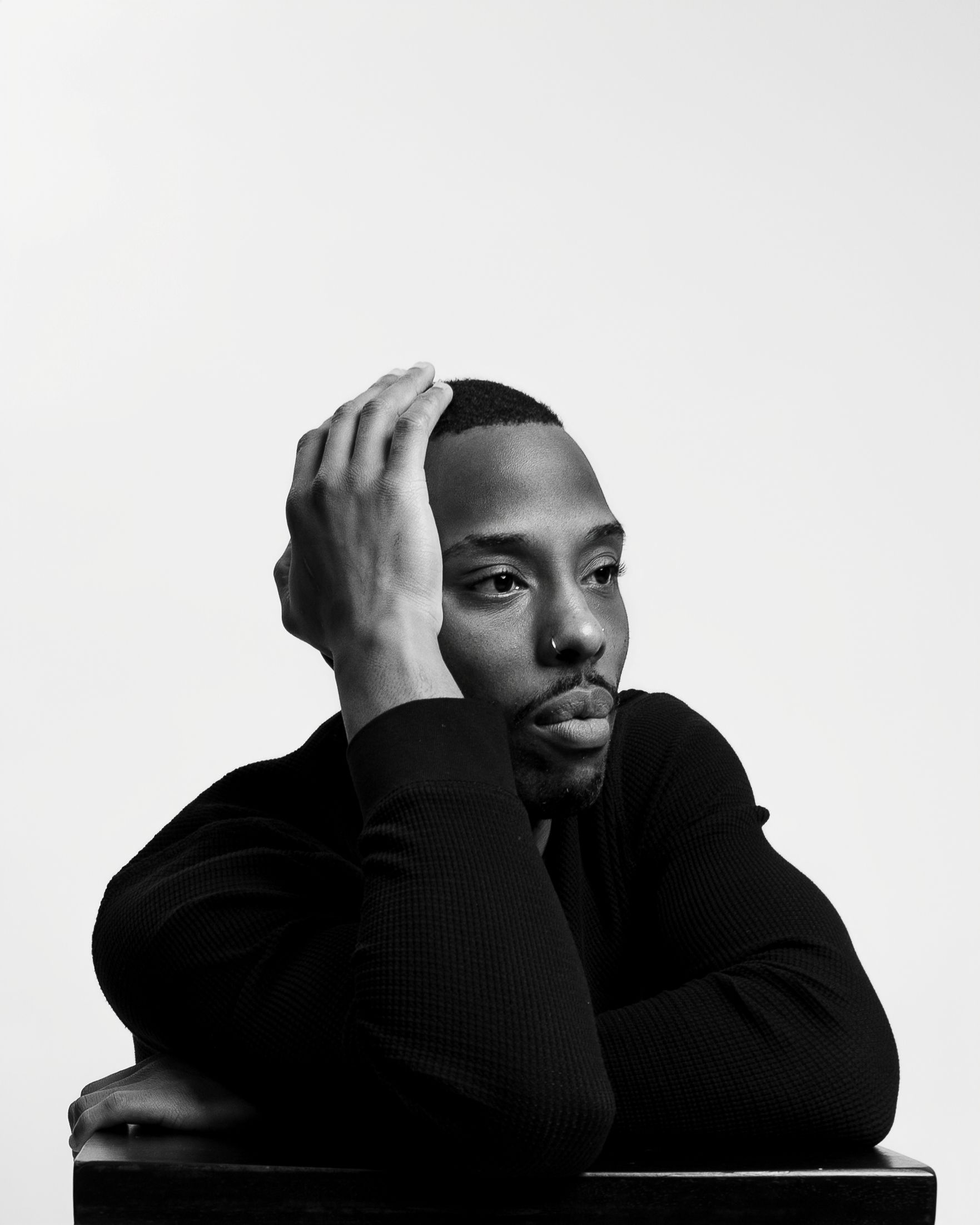 A black and white artistic portrait of a person in a dark sweater resting their head thoughtfully against their hand.