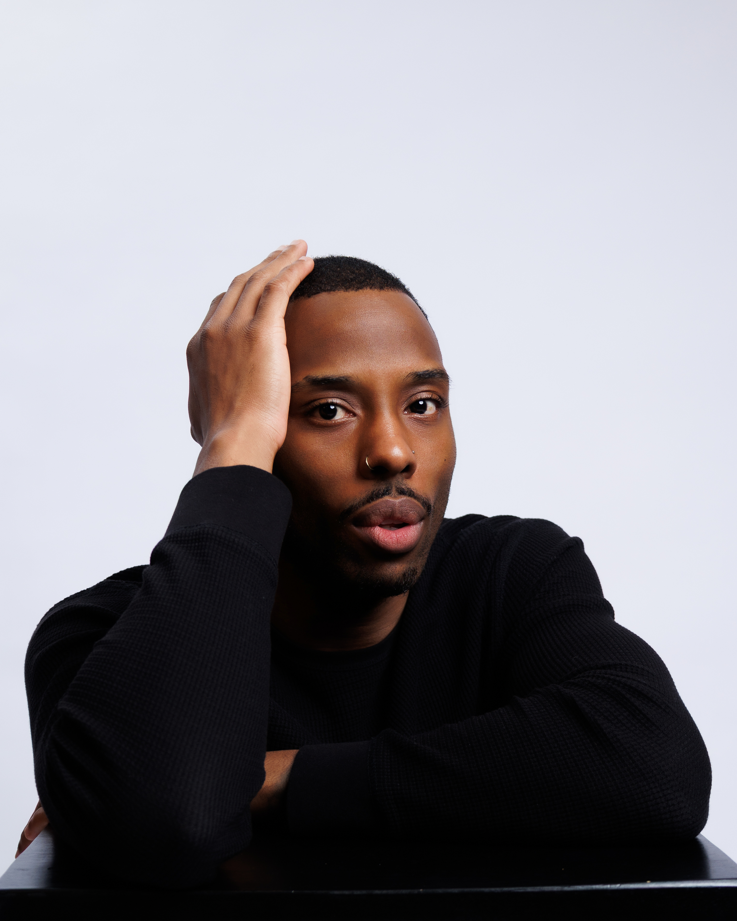 A person in a black sweater poses against a white background in a series of three similar shots.