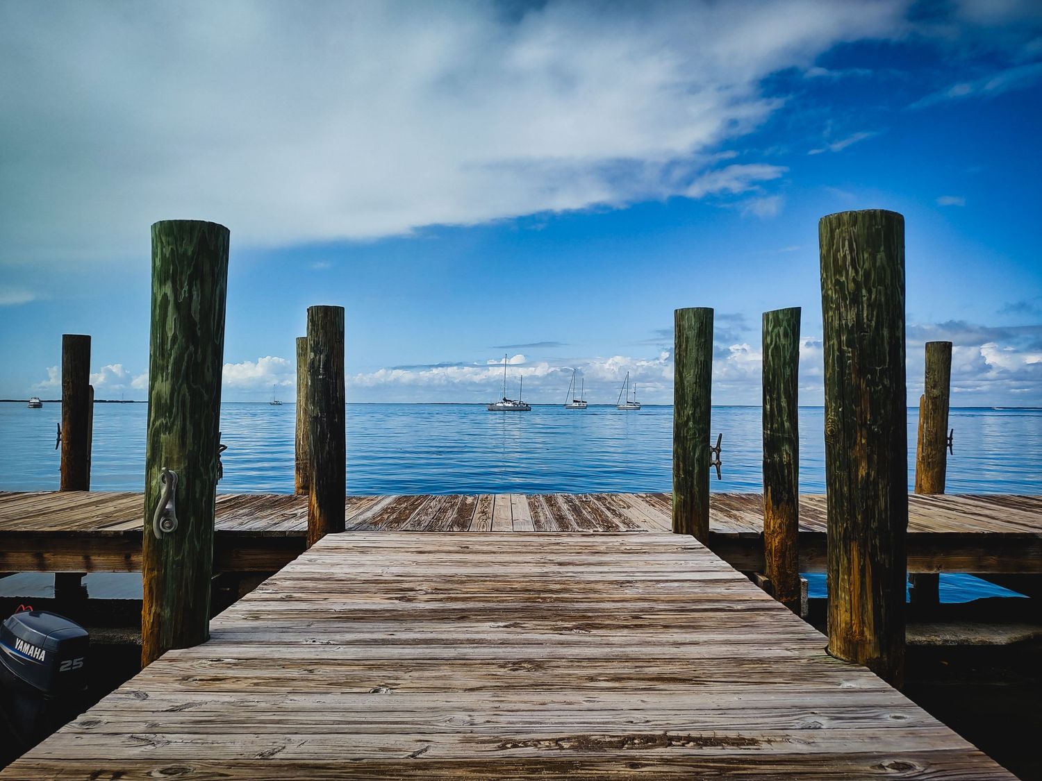 Three sailboats sit on calm blue waters with a weathered pier in the foreground in the Florida Keys