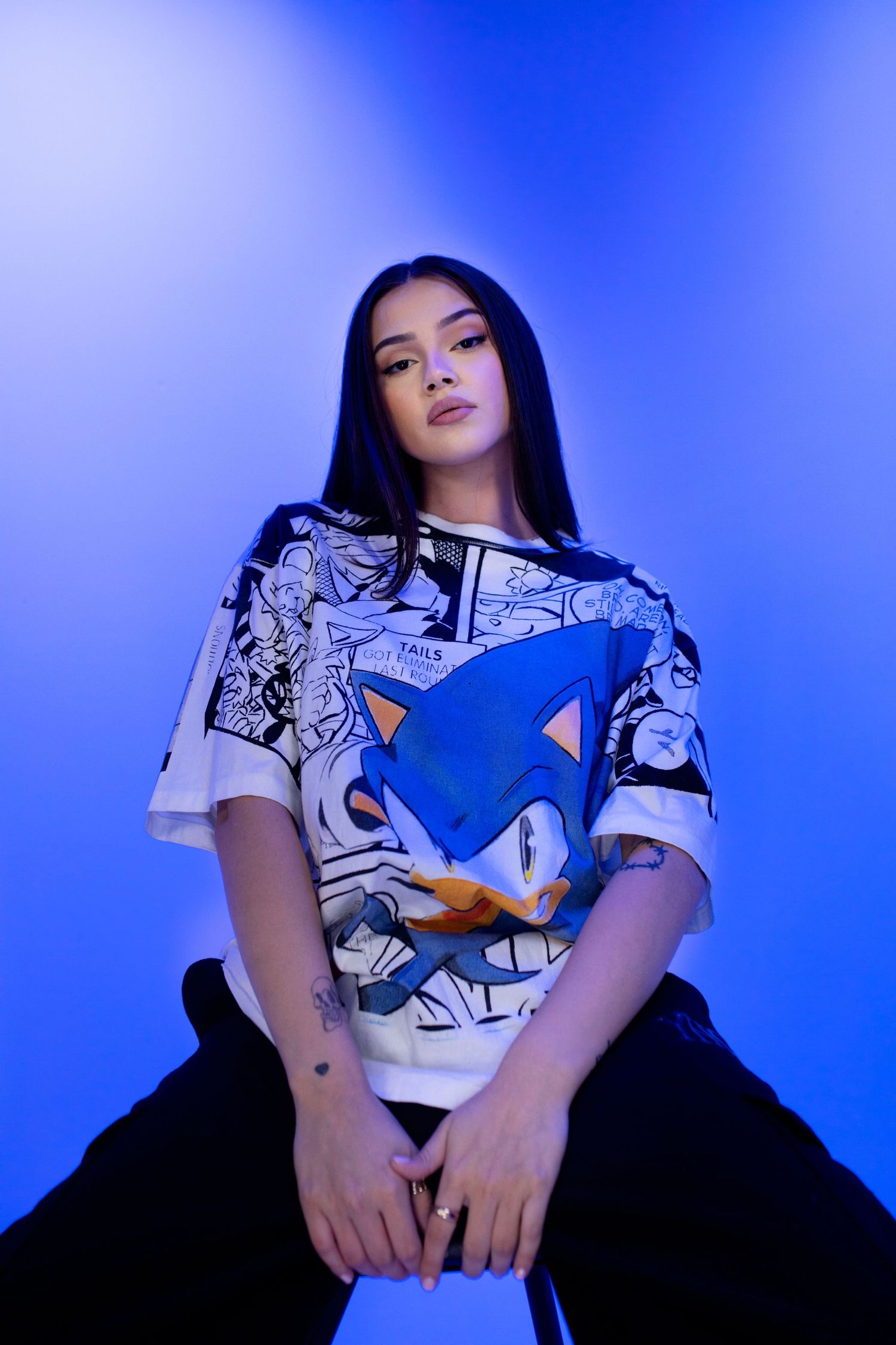 A person wearing a Sonic the Hedgehog graphic t-shirt poses against a vibrant blue background in a photo series.