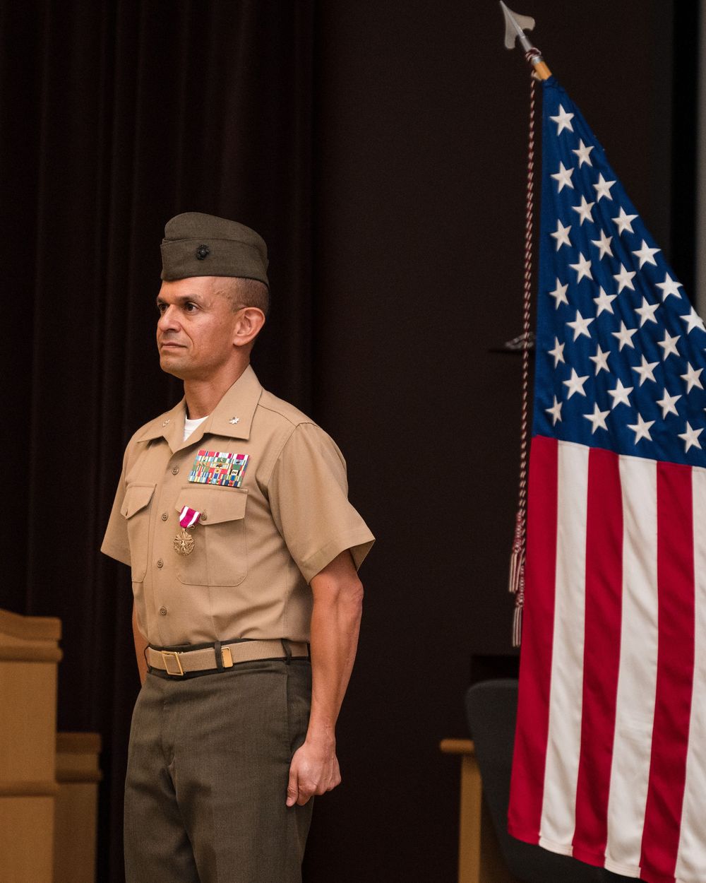 A uniformed Marine stands at attention next to an American flag during a formal military ceremony.