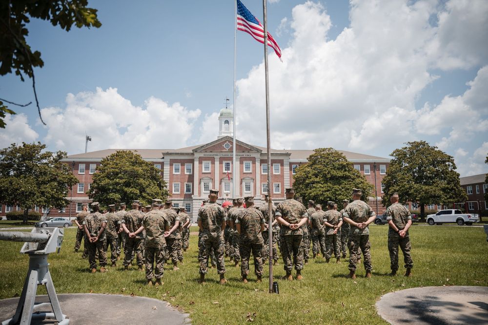 Military personnel gather on a lawn in front of a government building with an American flag flying above.