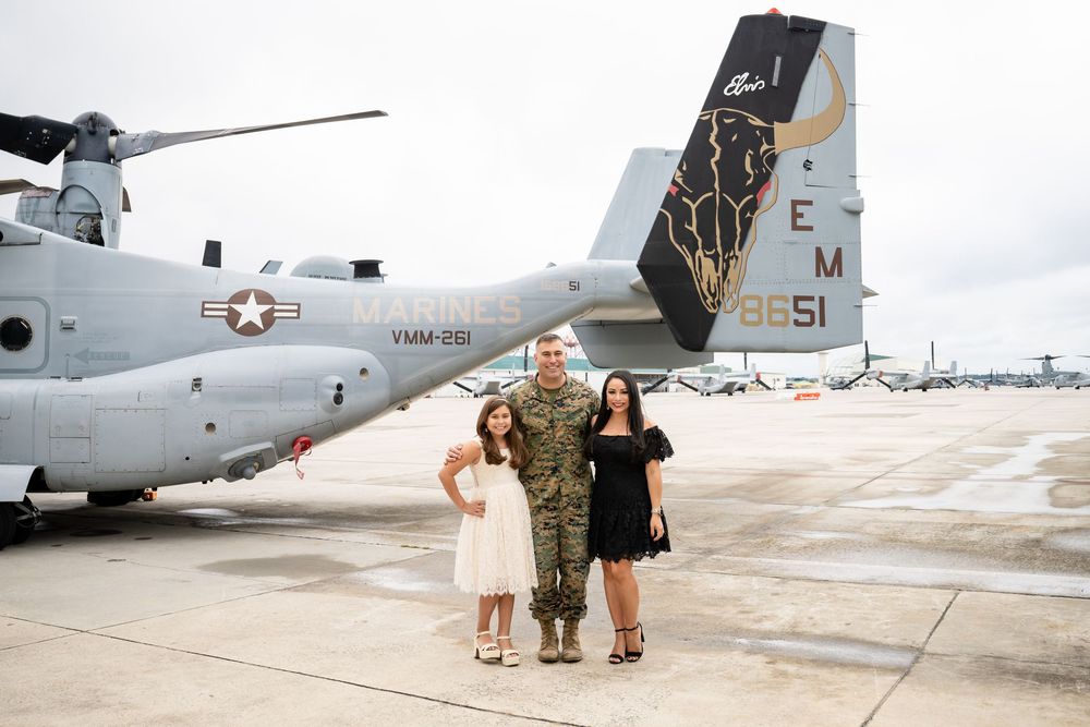 Military personnel and families gather near a large cargo aircraft on an airfield tarmac during a reunion scene.