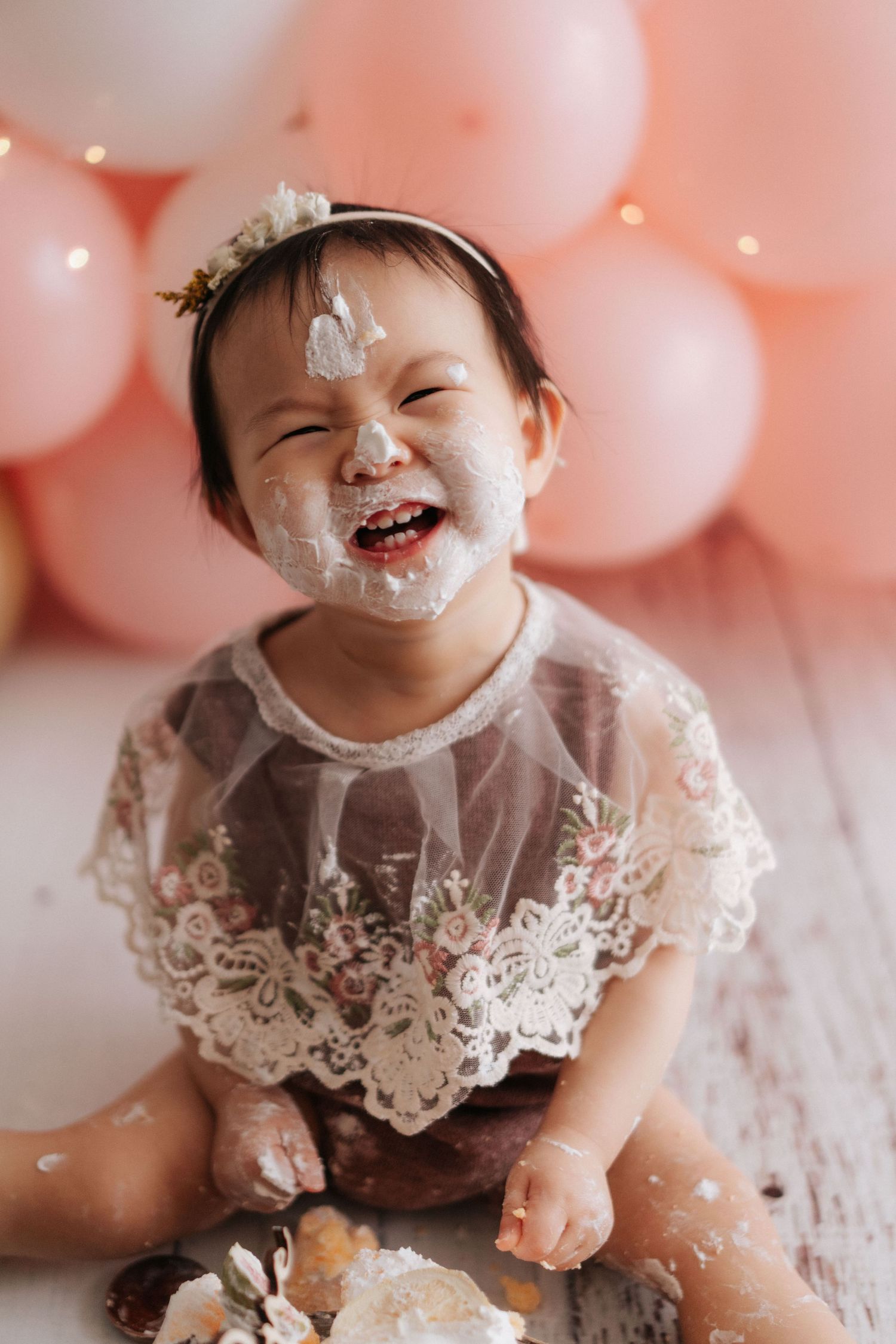Happy baby wearing knitted bunny hat and romper sits on floor with smashed cake during first birthday photo shoot.