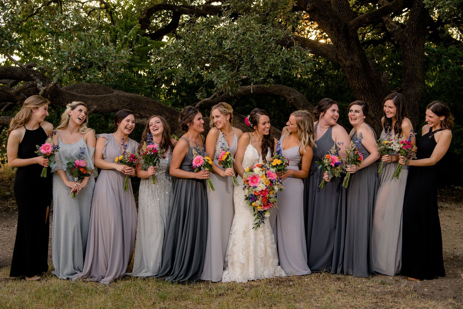 Wedding party in coordinated gray dresses poses together outdoors during sunset ceremony.